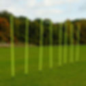 A cluster of six yellow poles arranged on a grassy surface, creating a vibrant contrast with the green grass.