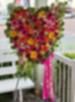 Heart-shaped standing funeral spray with red, pink, orange, and yellow roses, gerbera daisies, lilies, and lush greenery