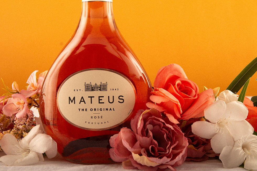 Vinho Matheus Rosé enquadrado mais a esquerda. Fundo amarelo. Garrafa entre flores.
