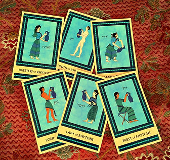 The six face cards from the suit of Rhytons, laid out casually on a red jacquard fabric background. The cards are all painted in shades of blue.