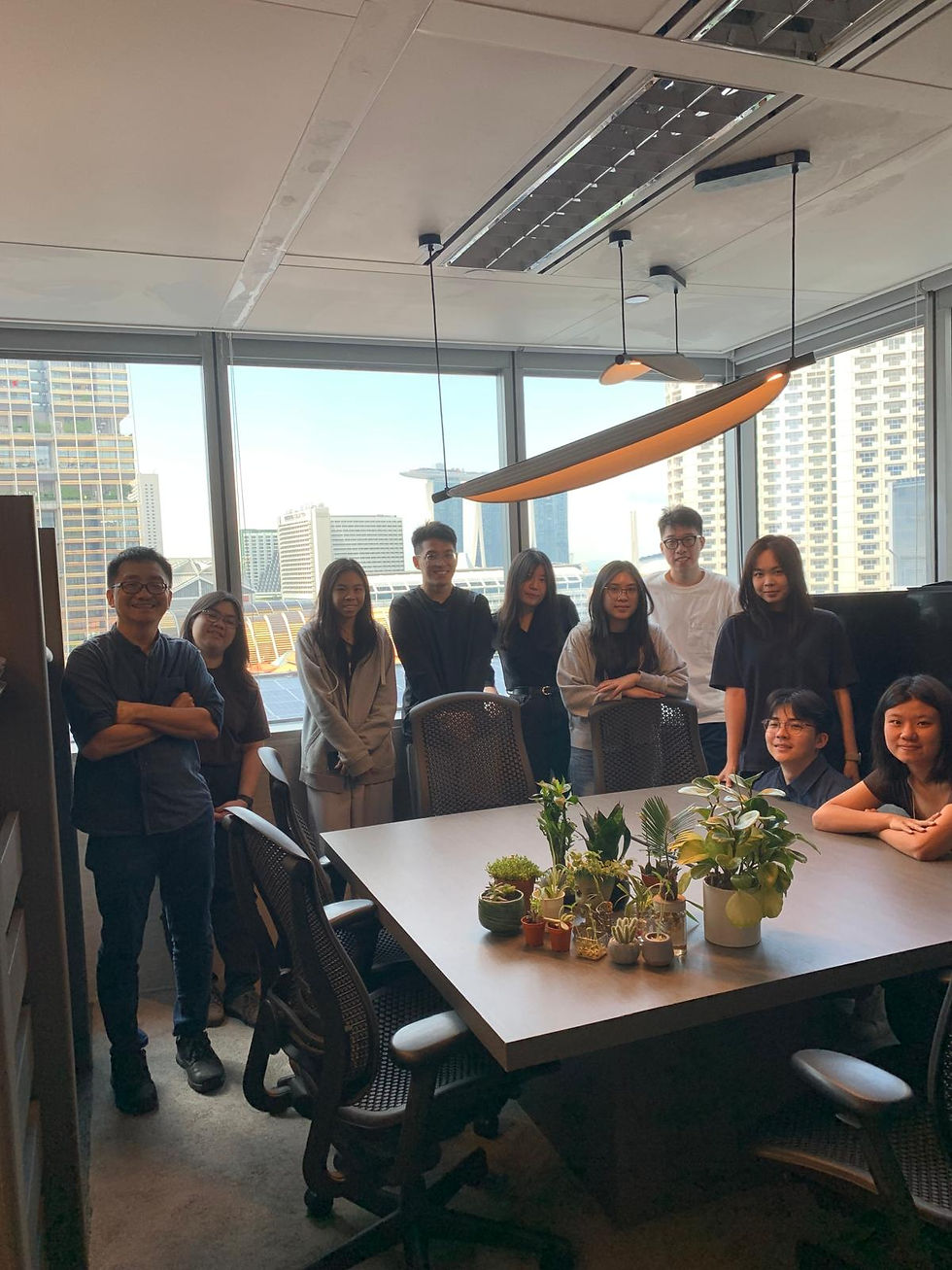 The Singapore ARTG team brings a potted plant into the office, smiling and celebrating Green Month together.