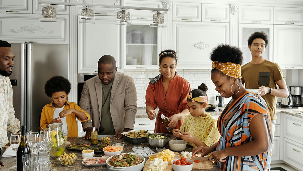 Diverse family preparing food together around a kitchen island in a bright white kitchen, smiling and chopping ingredients.