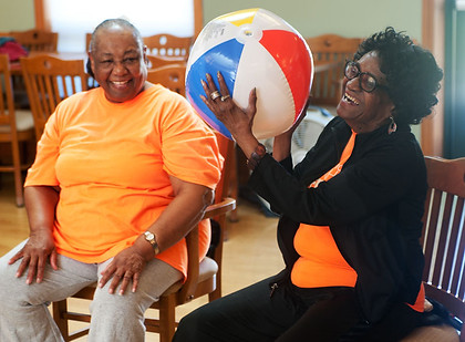 Two members laugh while tossing a beach ball during a fitness class