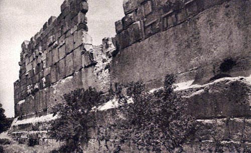 Back of the temple of Baal-Jupiter. Smaller stones of Roman date are haphazardly placed on top to form a medieval fortress. At the bottom of the picture, between the 2 trees, a man contemplates their size. Can you see how small he is compared?