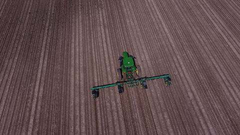 Photo aérienne d’un tracteur agricole vert avec un semoir en action dans un champ fraîchement labouré. Les lignes parallèles des sillons dessinent un motif géométrique précis, illustrant les techniques modernes de culture. Cette vue capturée par drone met en avant l’efficience des équipements agricoles dans la préparation des sols, essentielle pour une agriculture durable et productive.