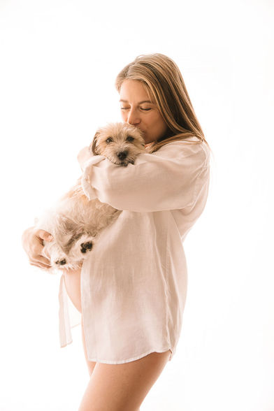Photographie studio à domicile d'une femme enceinte échangeant un doux baiser avec son chien, une expression d'amour et de complicité entre l'animal et sa maîtresse.