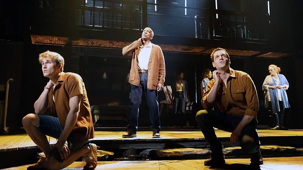 John Cardoza, Ryan Vasquez, and Dorian Harewood perform on a stage deck scenically finished as weathered planks of wood with a pool at the center in the Broadway production of The Notebook.