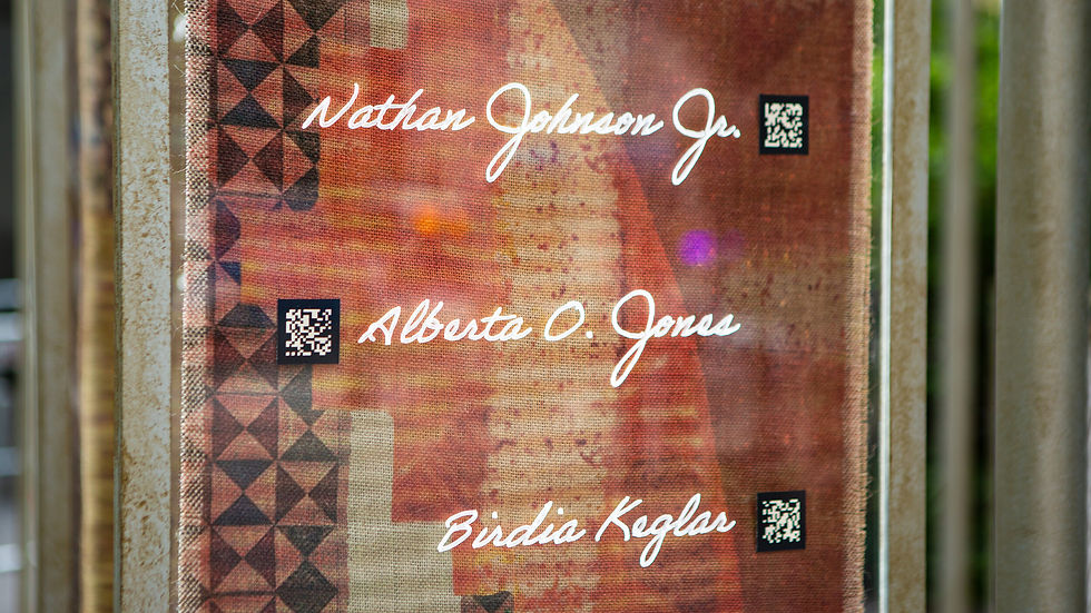 Names engraved on a glass pane in cursive with QR code stickers beside them and in front of a quilt print graphic, part of the pop-up AR art installation "Un(re)solved".