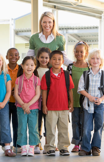 Smiling teacher and students stand together with backpacks at school.