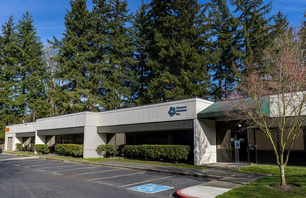 Exterior photo of 1 story commercial building. Tall, trees are behind the building and hedges are in front.
