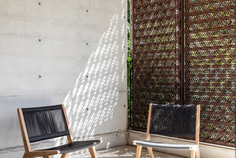 Two outdoor chairs set against a concrete wall, with sunlight patterned through a decorative metal mesh screen.