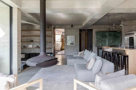 Open-plan living space with exposed concrete, suspended fireplace, modular seating, and kitchen with timber island.