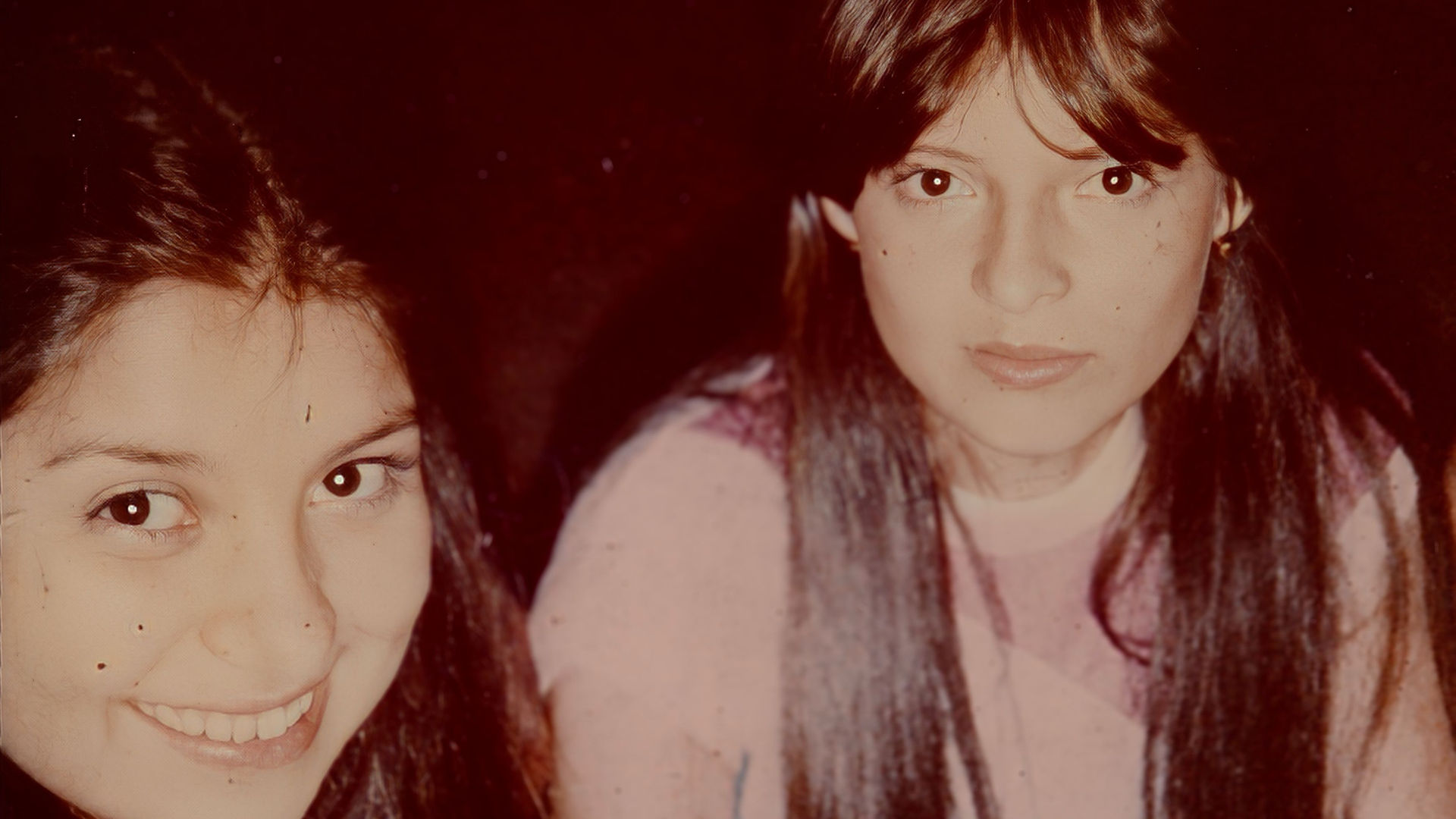 Photo of Marta Campos-Mace and Norol as teenagers, both with long dark hair, smiling at the camera. Their friendship is mentioned in Part One and Part Two of Invisible Grounds.