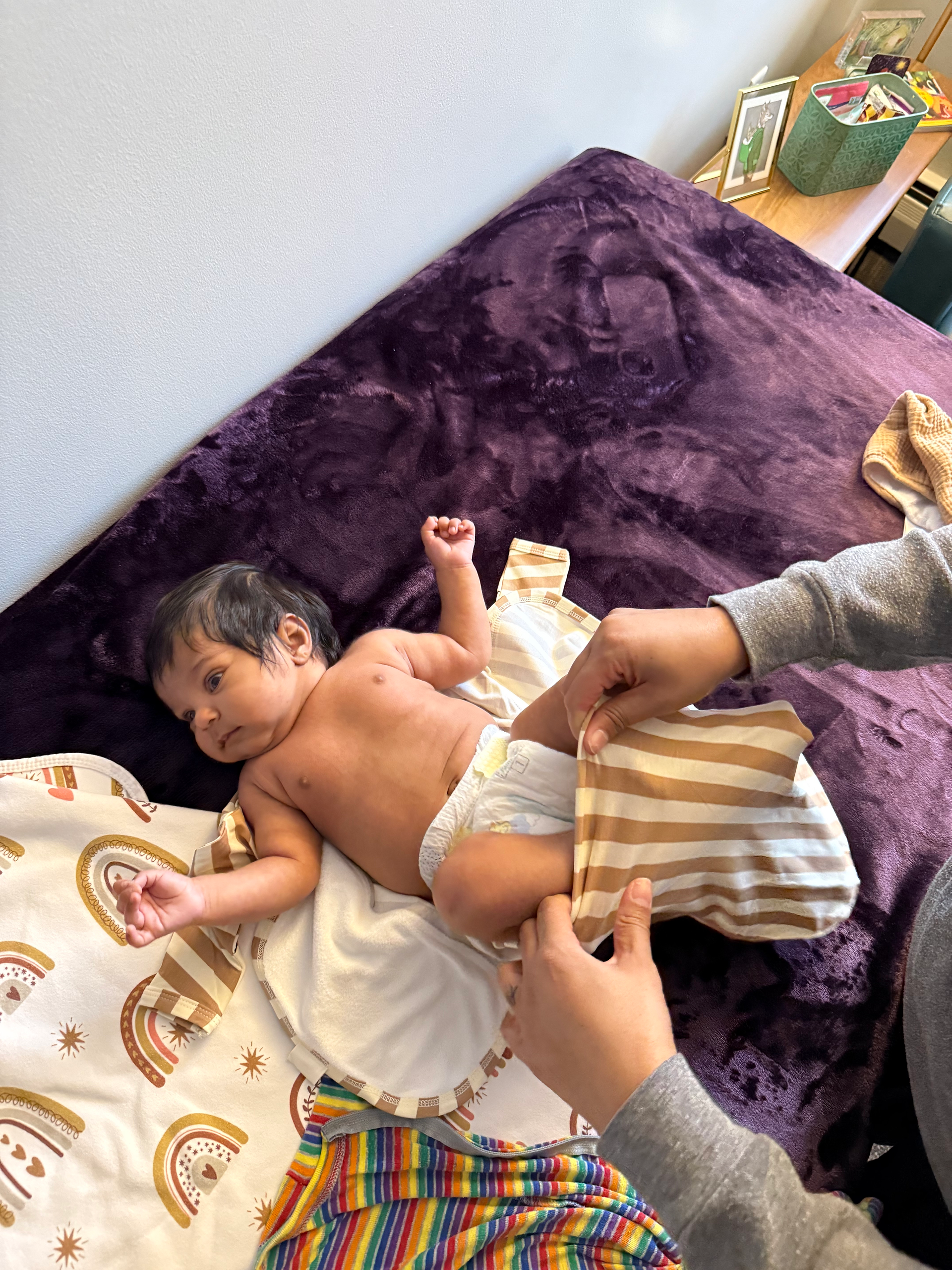 Infant on a purple blanket being dressed in a striped gown