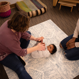 woman in purple shirt assisting baby on may next to mother on the floor