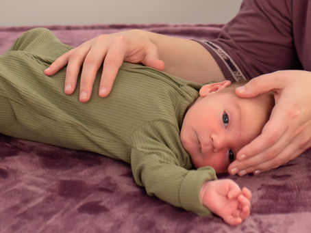 baby in a green footie looking at the camera with gentle hands on head and abdomen, photo credit: Kate's Takes 