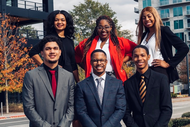 Michael poses with five other students of the Collegiate 100. All are formally dressed in suits.