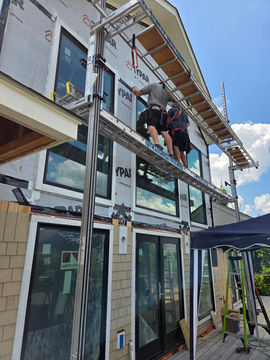 Contractors on scaffolding installing windows on a house.