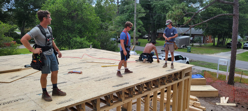 Four construction workers on a wooden house floor frame.