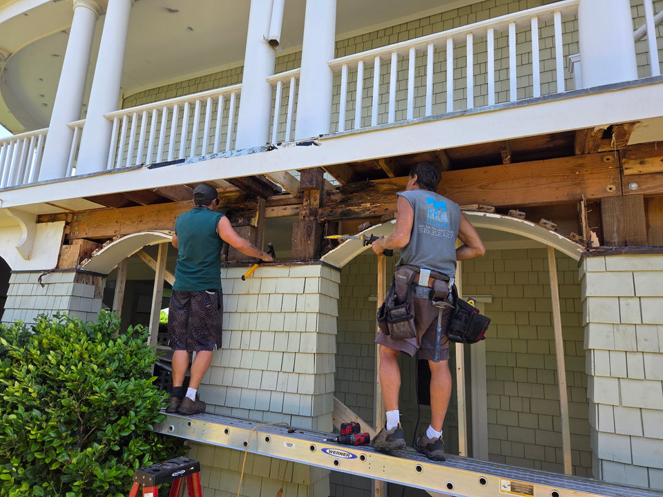 Two workers repairing the structural frame of a porch.
