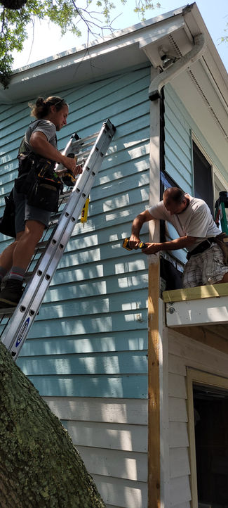 Two workers repairing light blue house siding on ladders