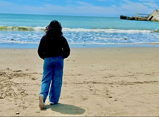 Girl in baggy jeans and a sweatshirt facing towards the beach