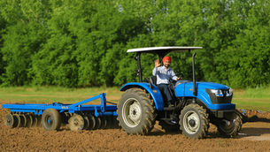 Hombre conduciendo su tractor Solis adquirido en GERDOM, traabajando la tierra en el campo con su arado de 20 discos