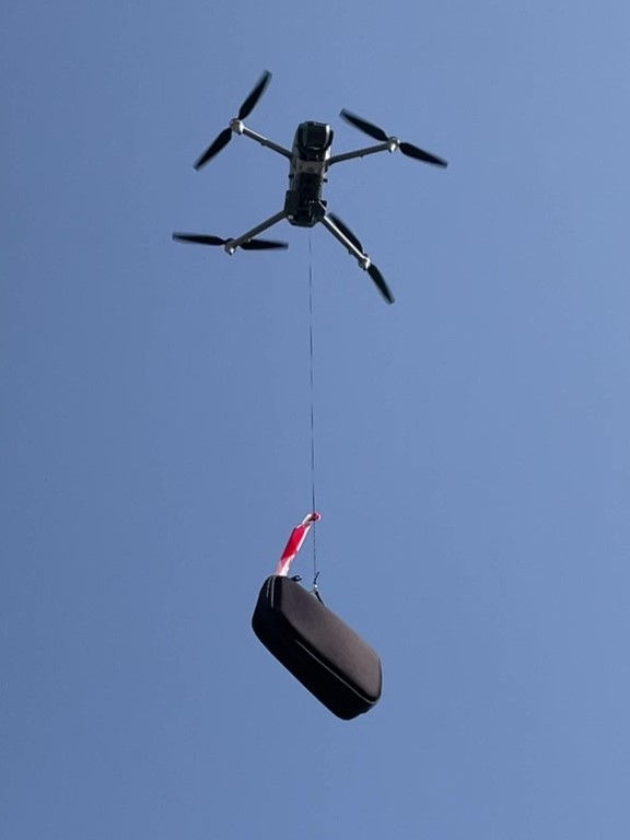 Thumbnail: Aerial shot of Matrice 4E drone with Sky Hook transporting package across wide outdoor environment
