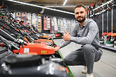 a customer examines new models of lawn mowers in an electrical store for gardeners and hor