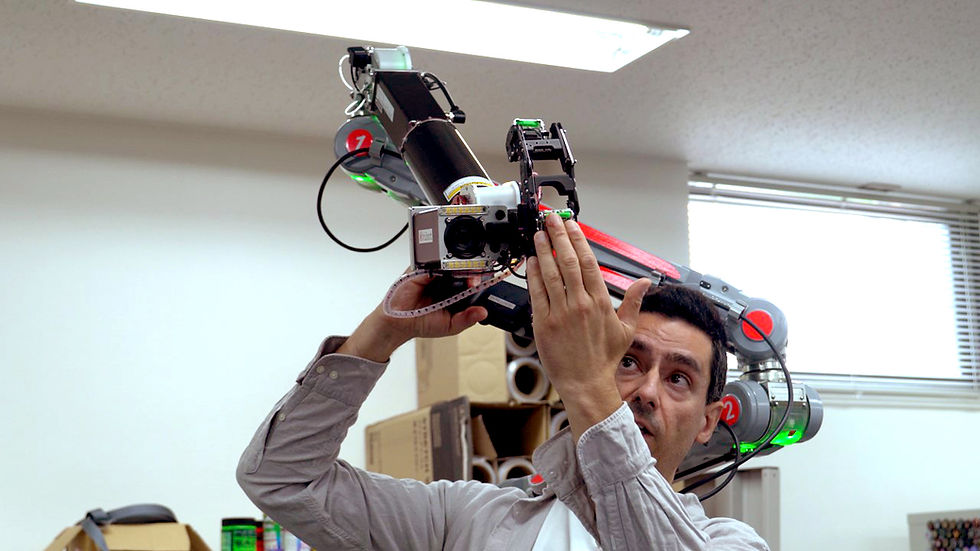 Man adjusts a robotic arm with cameras and colored lights in an office. Boxes in the background. Focused expression. Fluorescent lights above.