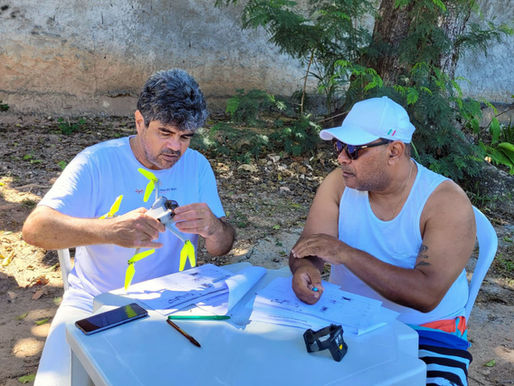Instrutor de drone em Salvador mostrando detalhes técnicos das hélices e sensores de um drone cinza para um aluno atento em aula prática ao ar livre.
