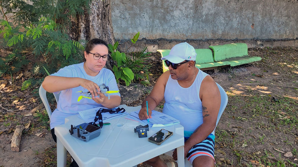 Instrutora manuseando um drone DJI com hélices amarelas, explicando a montagem para um aluno que faz anotações em uma apostila técnica.