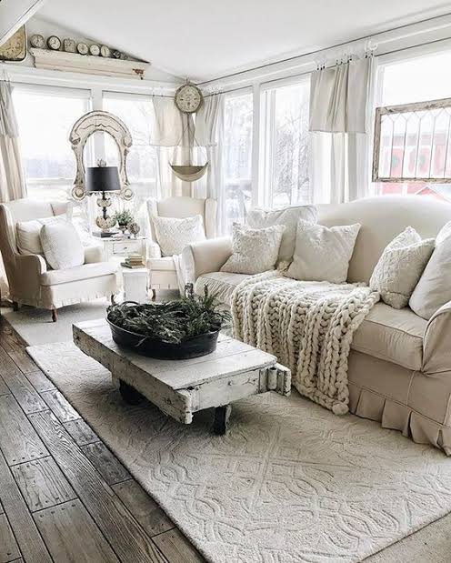 A cozy and stylish living room with bright blue and white traditional Greek island architecture visible through large windows. The interior features a modern orange and white sofa, elegant gold floor lamps, a wooden coffee table, and a bookshelf filled with books. Blue accents and Mediterranean elements create a warm, inviting atmosphere. This image was generated using ArchiVinci AI.