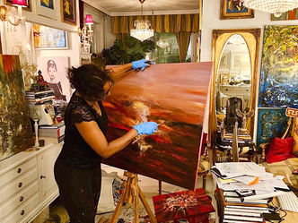 The artist in her studio, painting the abstract acrylic
piece Crimson Dreams amid a collection of her work, capturing the intensity of sunrises and sunsets inspired by a lifelong nomadic spirit.