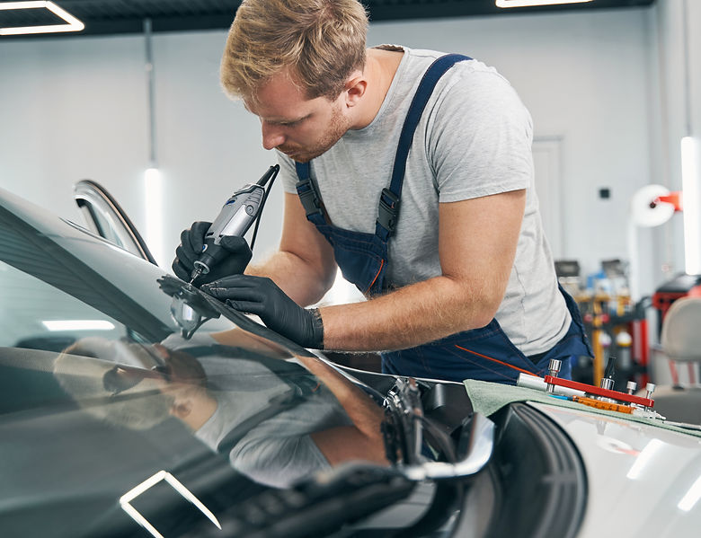 Car service technician checks crack on car windshield closeup
