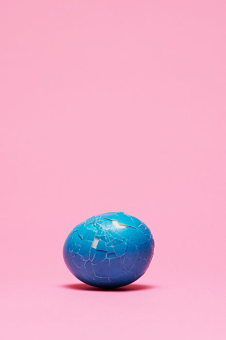 blaues und angeschlagenes Osterei auf rosa Hintergrund