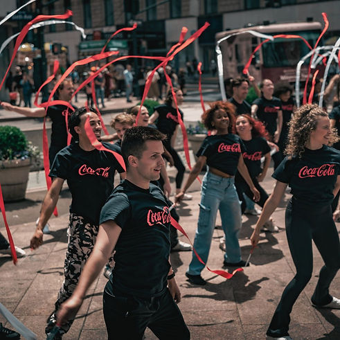 Flash mob dancing in Herald Square Park with streamers and branded coca-cola shirts