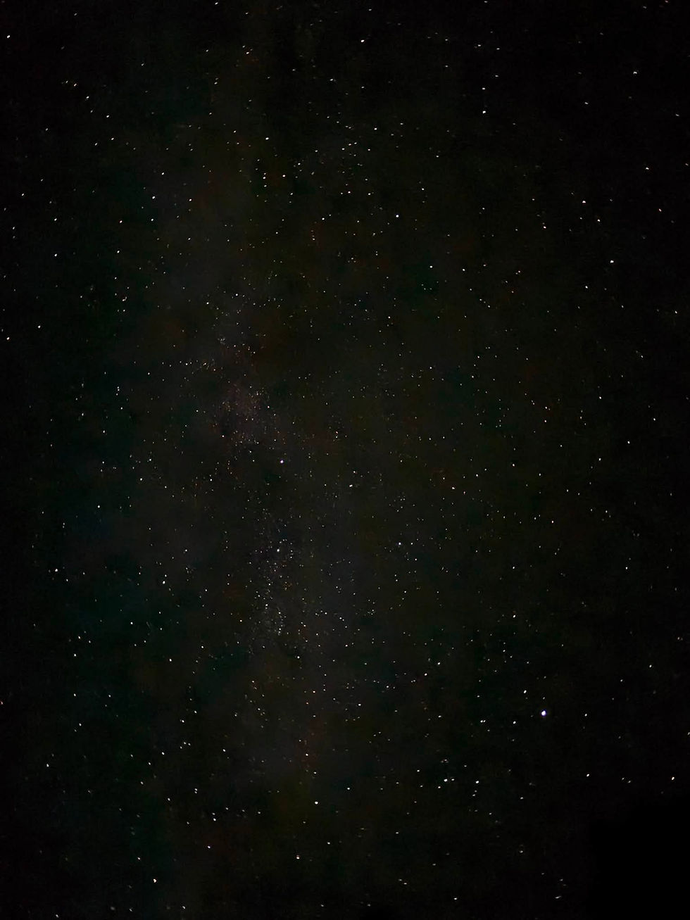 Star-filled night sky with a faint greenish nebula or Milky Way band against a dark black background.