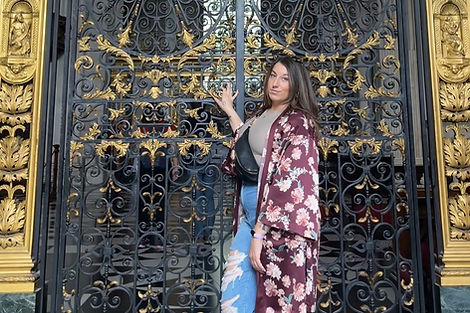 woman standing in front of ornate gate, wearin the Alex sling bag in black