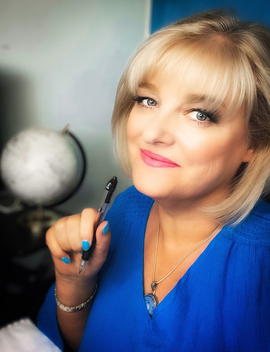 a photo of Shelley Watson, short blonde hair, blue shirt, holding pen, with globe in background
