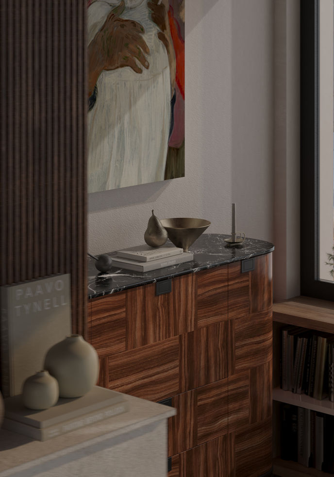 A close-up interior detail showing a wooden sideboard with a black marble top, decorated with sculptural objects, books, and a metallic bowl. A large painting partially visible above it, with soft natural light entering from the right