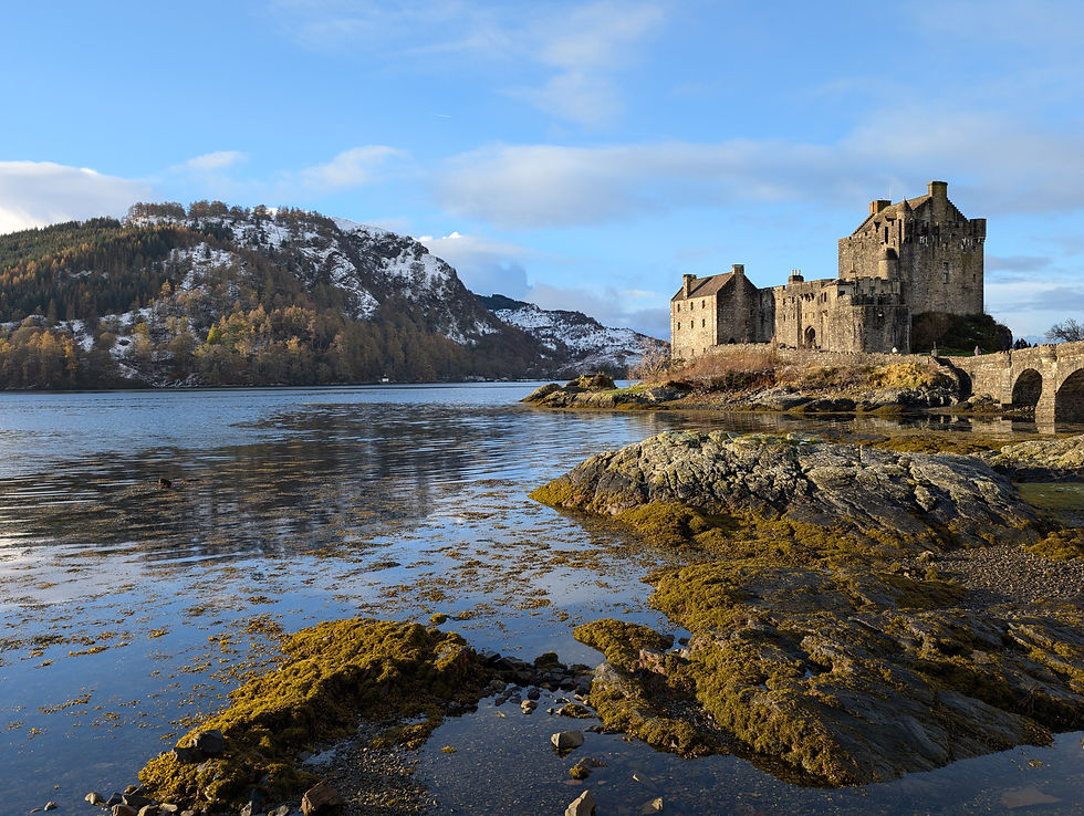 Eilean Donan Castle stands majestically by the water's edge against a backdrop of snow-dusted hills and a clear blue sky, exemplifying Scotland's picturesque landscape.