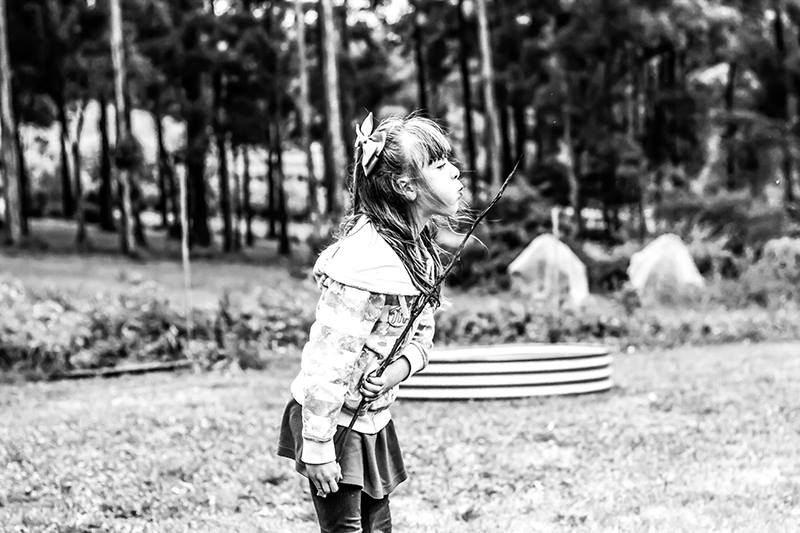 Black and white image of a young girl whose hair is blowing in the wind. She is holding a stick and blowing on it to blow out the flame.
