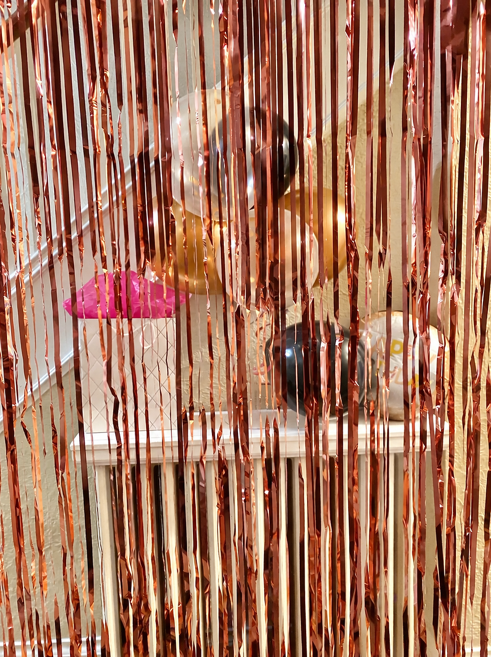 Rose gold party streamers with birthday decorations behind them