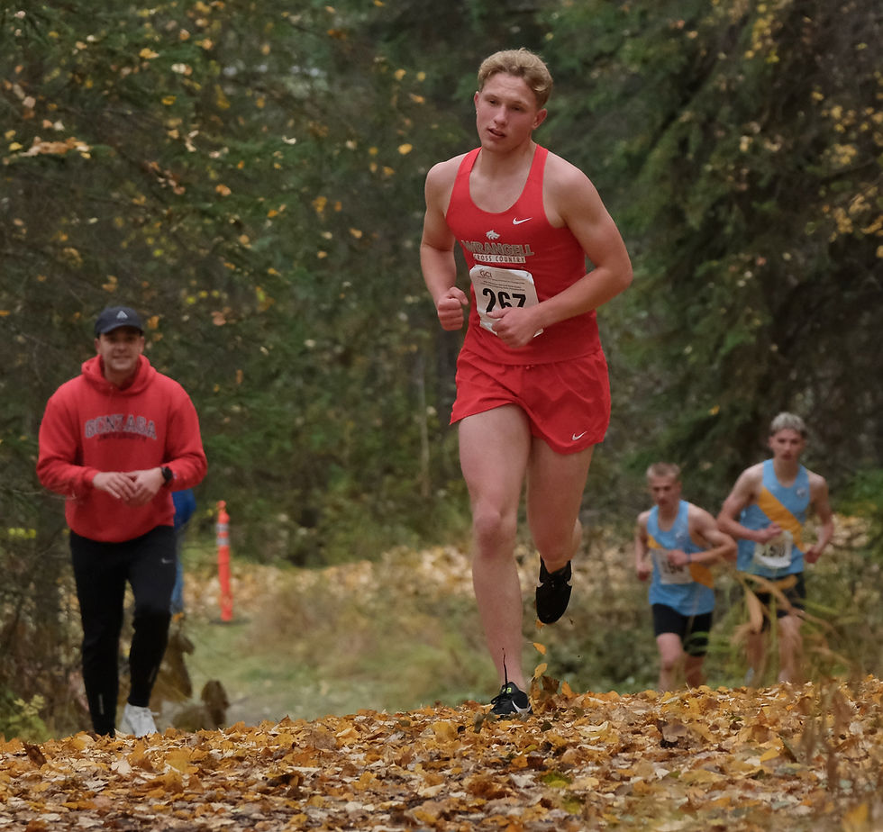 Wrangell senior Jackson Carney powers up a hill in front of two Dillingham runners as coach Mason Villarma cheers during the Division III Alaska State XC Championships at Anchorage's Bartlett High School trails on Saturday, Oct. 3, 2026. Carney placed second in 17:57 and the Wolves were runner-up to Dillingham in the team scoring. Craig senior Aulis Nelson won the boys title in 16:41. (Klas Stolpe / Juneau Independent)