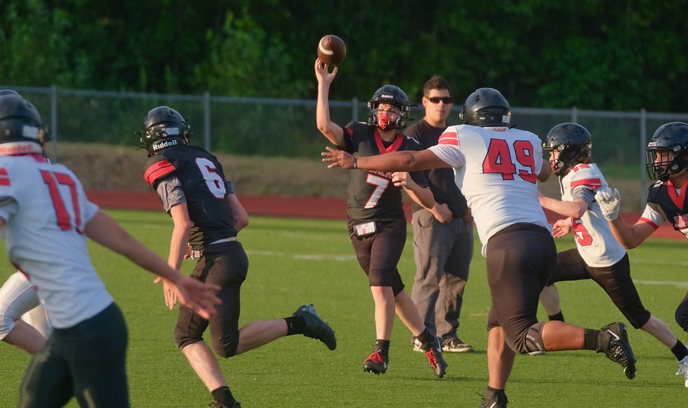 Juneau-Douglas High School: Yadaa.at Kalé sophomore Parker Katasse (7) looks to pass to sophomore Hendrik Van Kirk (6) under pressure from juniors Helaman Aitaoto-Tele'a (49) and Beckham Kasler (15) during the Crimson Bears scrimmage at Thunder Mountain Middle School's Falcons' Field on Monday, August 10, 2026. (Klas Stolpe / Juneau Independent)