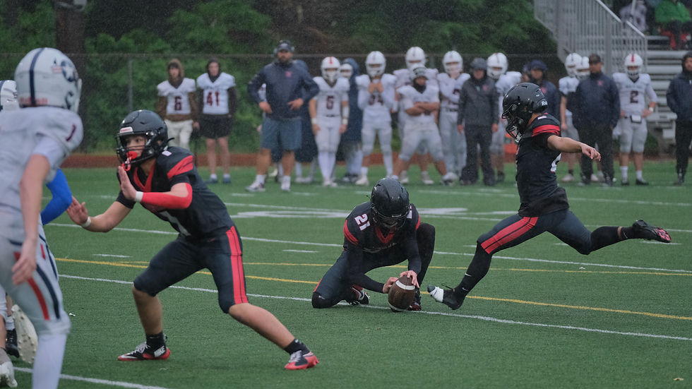 Juneau-Douglas High School: Yadaa.at Kalé senior kicker Sonny Mazon (2) hits and extra point as sophomore Carter Day (1) blocks and junior Andrew Sanders (21) sets the ball during the Crimson Bears' 52-0 win over the Patriots at Adair-Kennedy Memorial Park field on Saturday, Aug. 29, 2026. (Klas Stolpe / Juneau Independent)