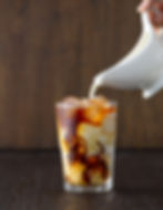 ice coffee in a glass cup with cream being poured into it