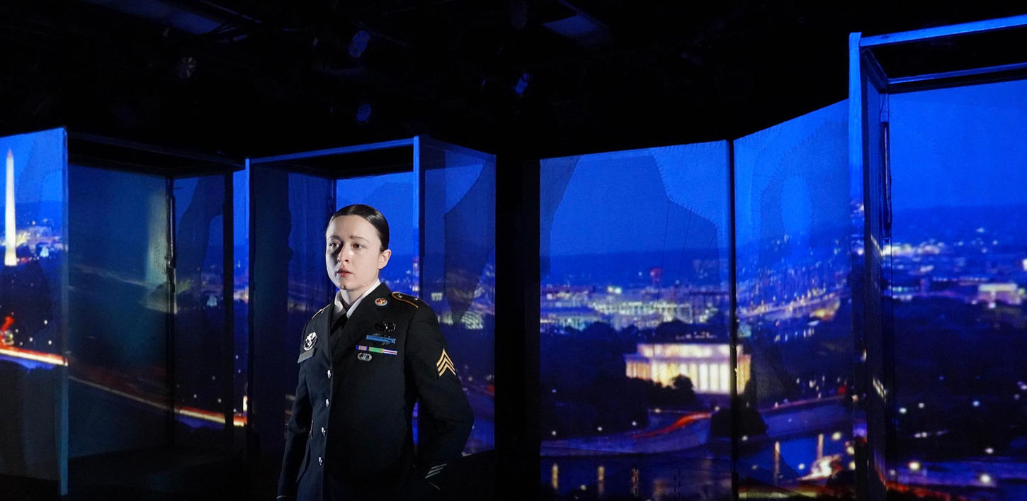 Production photo of a woman in front of scenery that has a projection of a city on it