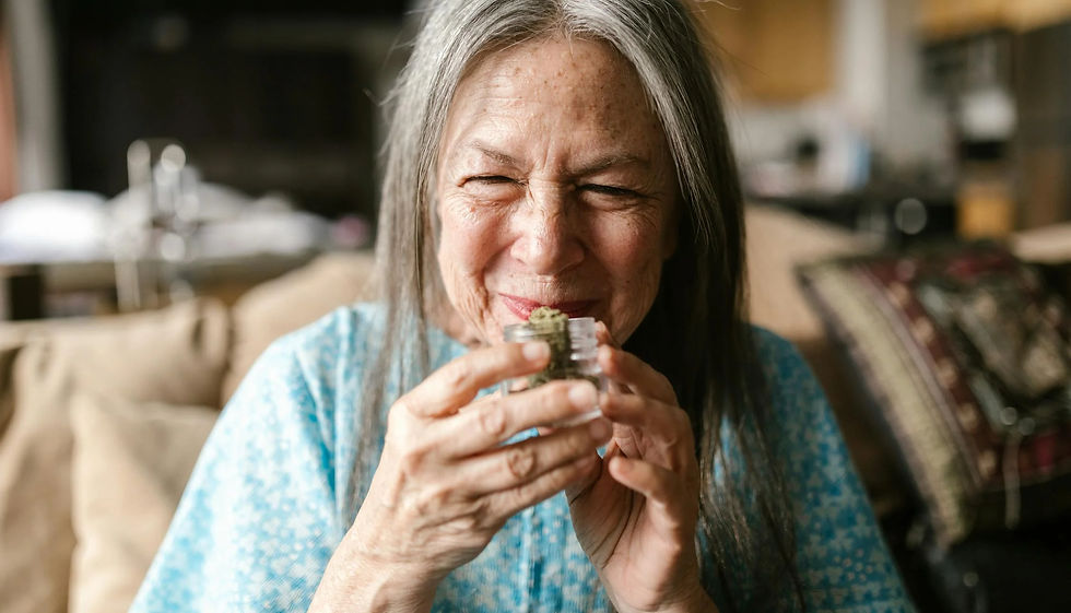Older woman smiling and enjoying the aroma from a jar of cannabis, sitting looking happy.